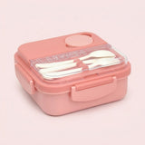 A pink plastic lunch box with a clear lid, containing white utensils, set against a solid pale pink background.