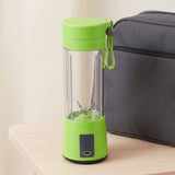 A portable electric blender with a bright lime green lid, base, and carrying strap, shown on a light wood table next to a dark gray bag.