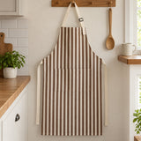 Full-length brown striped kitchen apron shown beside a mug and wooden spoon for everyday scale.