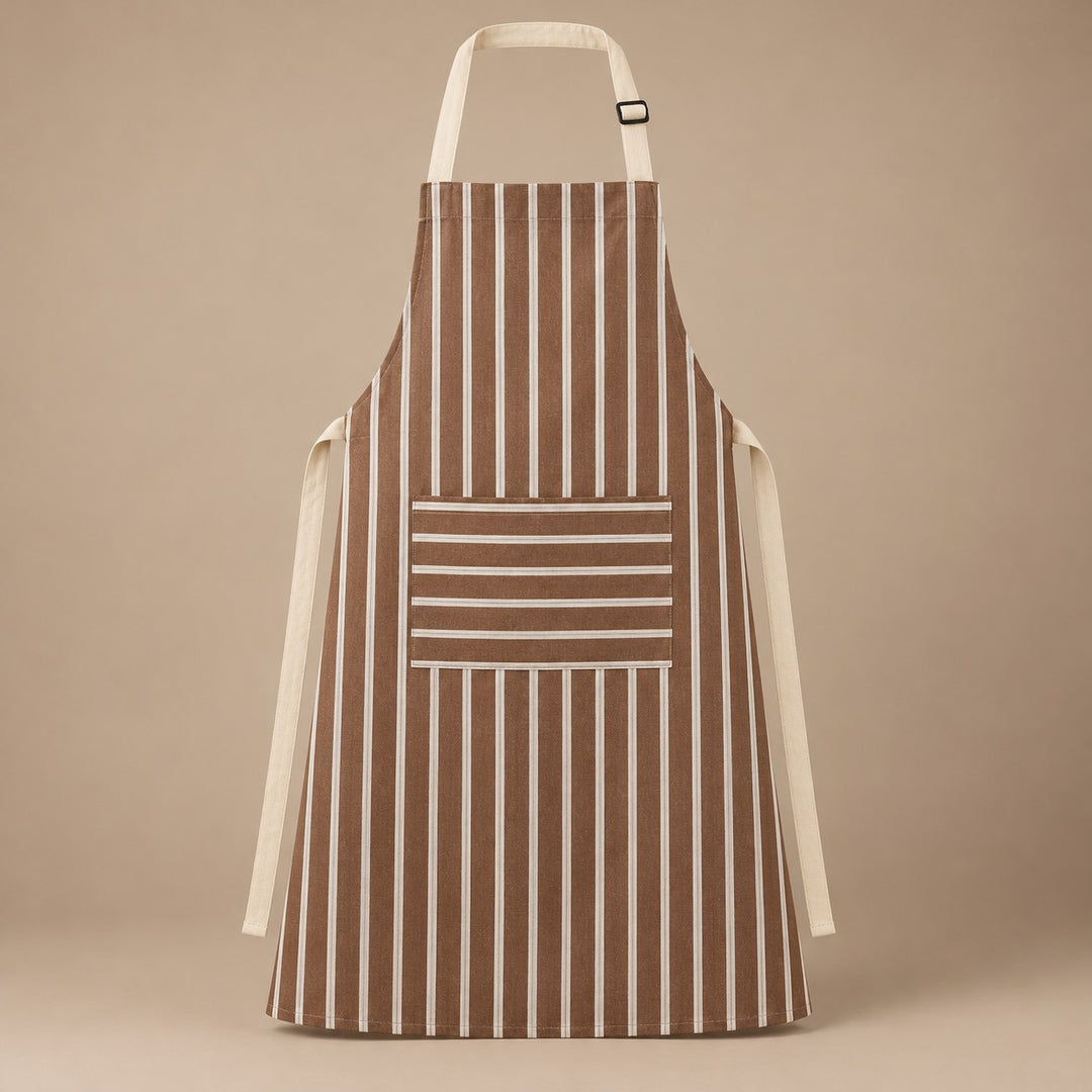 Brown striped kitchen apron with a horizontal pocket and adjustable straps on a warm studio backdrop.