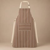 Brown striped kitchen apron with a horizontal pocket and adjustable straps on a warm studio backdrop.