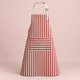 Red striped kitchen apron with a horizontal pocket and adjustable straps on a soft red studio backdrop.