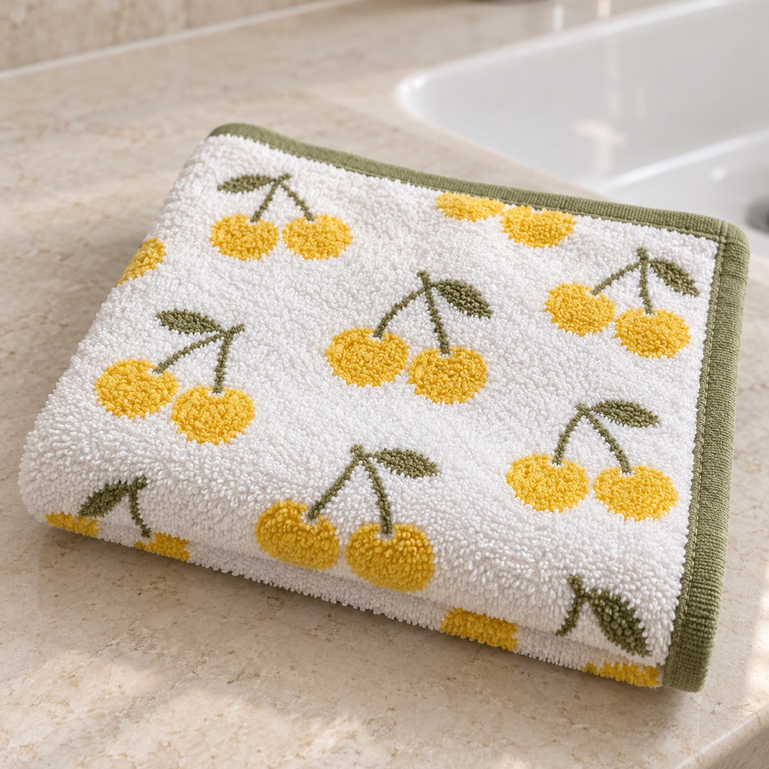 Cherry Print Cotton Washcloth folded on a bathroom counter, showing its cheerful pattern and terry texture.