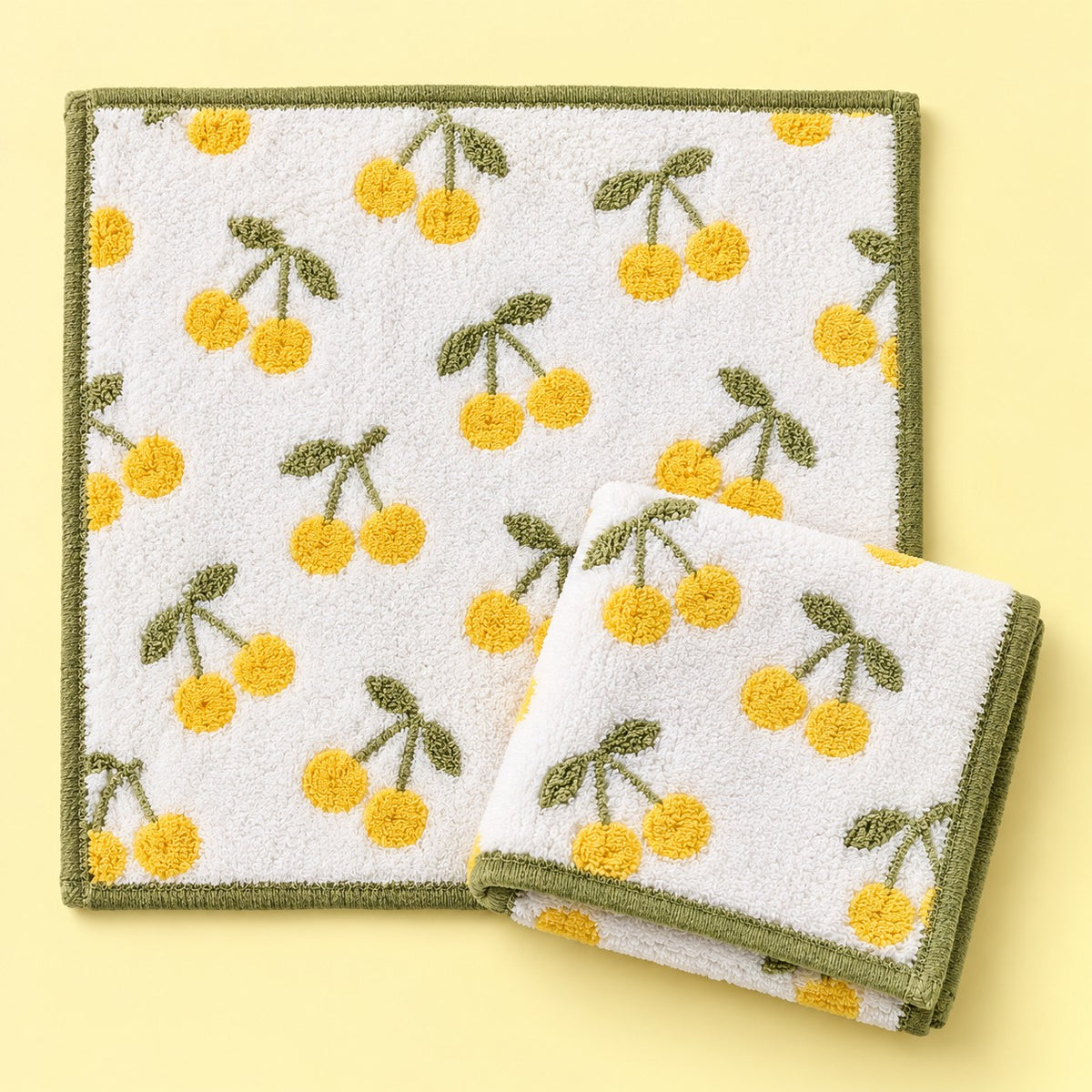 Two yellow cherry print cotton washcloths shown on a pale yellow studio background.