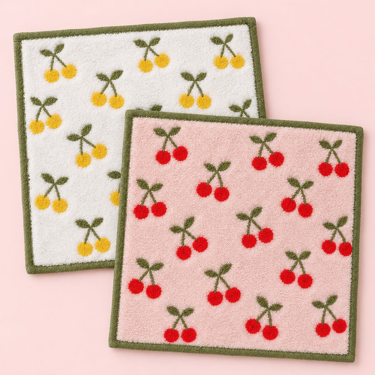 One yellow and one red cherry print cotton washcloth shown on a pale pink studio background.