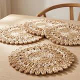 Three round woven straw placemats with scalloped edges arranged on a light wood table, with part of a wooden chair visible in the background.