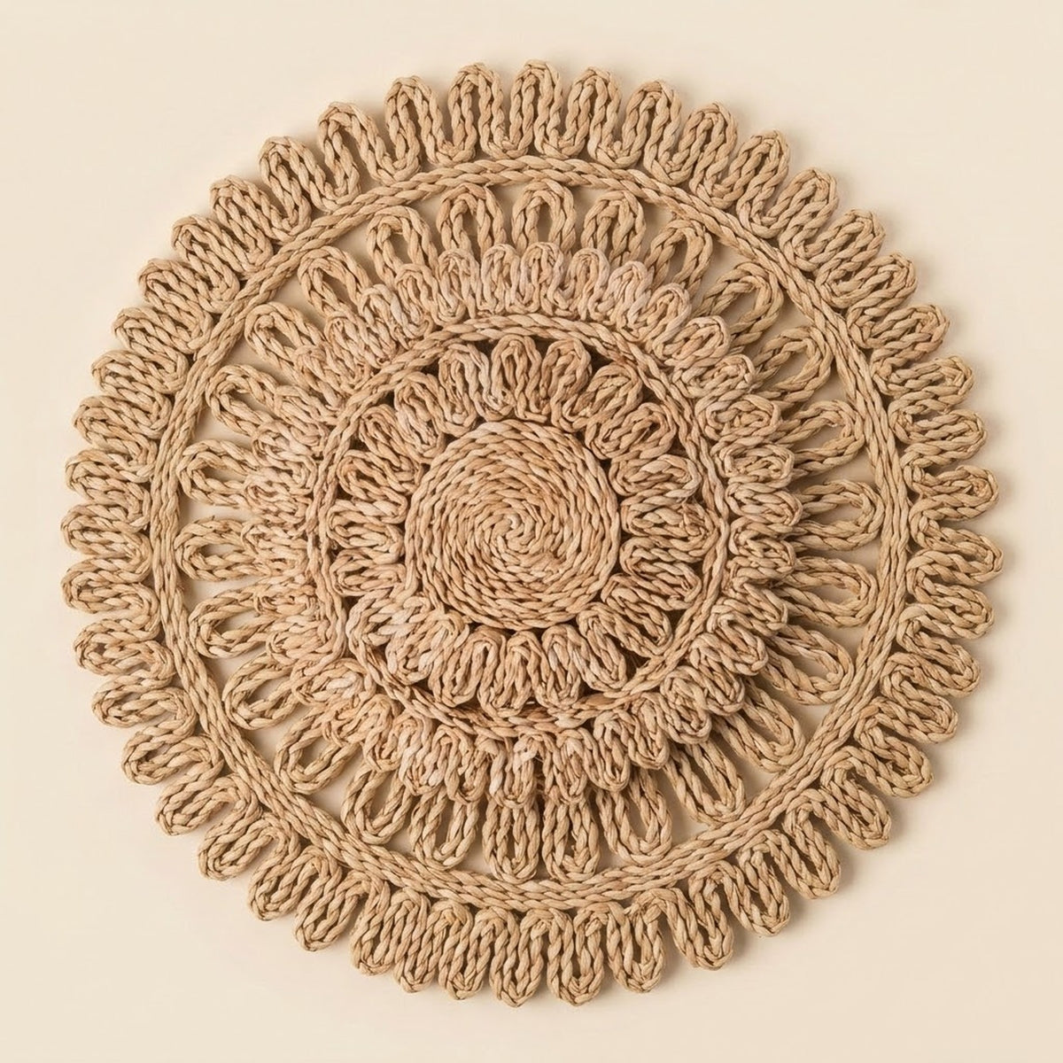 A round, handwoven jute placemat with a detailed concentric circular pattern and fringed edges, displayed flat against a solid cream background.