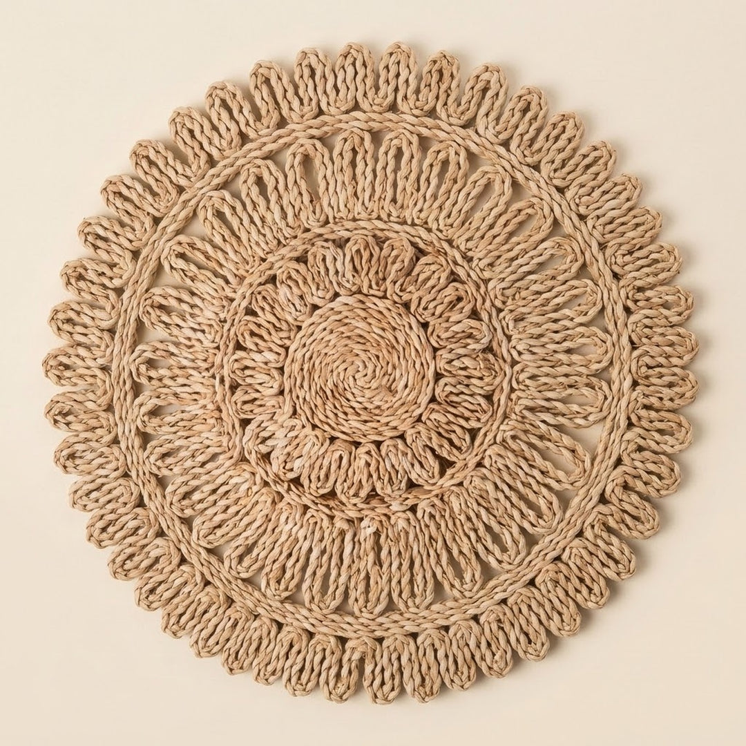A round, handwoven jute wall hanging or decorative mat with concentric circular patterns and a scalloped outer edge, shown flat against a solid light beige background.
