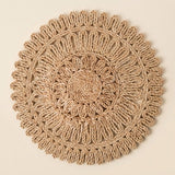 A round, handwoven jute wall hanging or decorative mat with concentric circular patterns and a scalloped outer edge, shown flat against a solid light beige background.