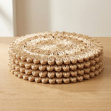 A stack of round woven seagrass coasters with a textured bumpy edge, displayed on a light wood tabletop against a neutral beige background.