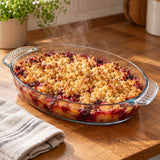 Oval glass baking dish holds a steaming fruit crumble on a kitchen counter, ready to serve.