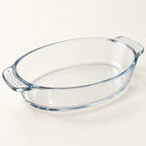 Clear oval glass baking dish highlights its thick curved handles and transparent, glossy finish.