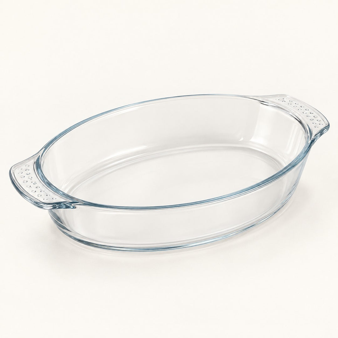 Oval clear glass baking dish shown alone on a soft ivory studio background.