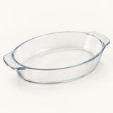 Oval clear glass baking dish shown alone on a soft ivory studio background.
