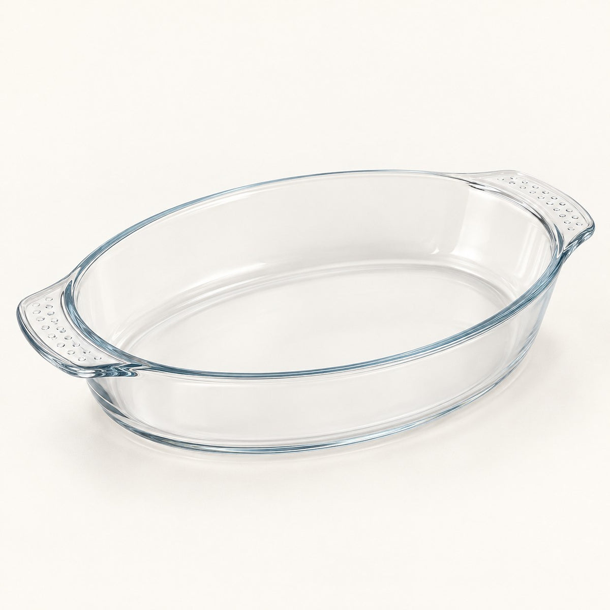 Oval clear glass baking dish shown alone on a soft ivory studio background.