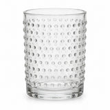 One clear embossed dot drinking glass stands alone against a pure white background.