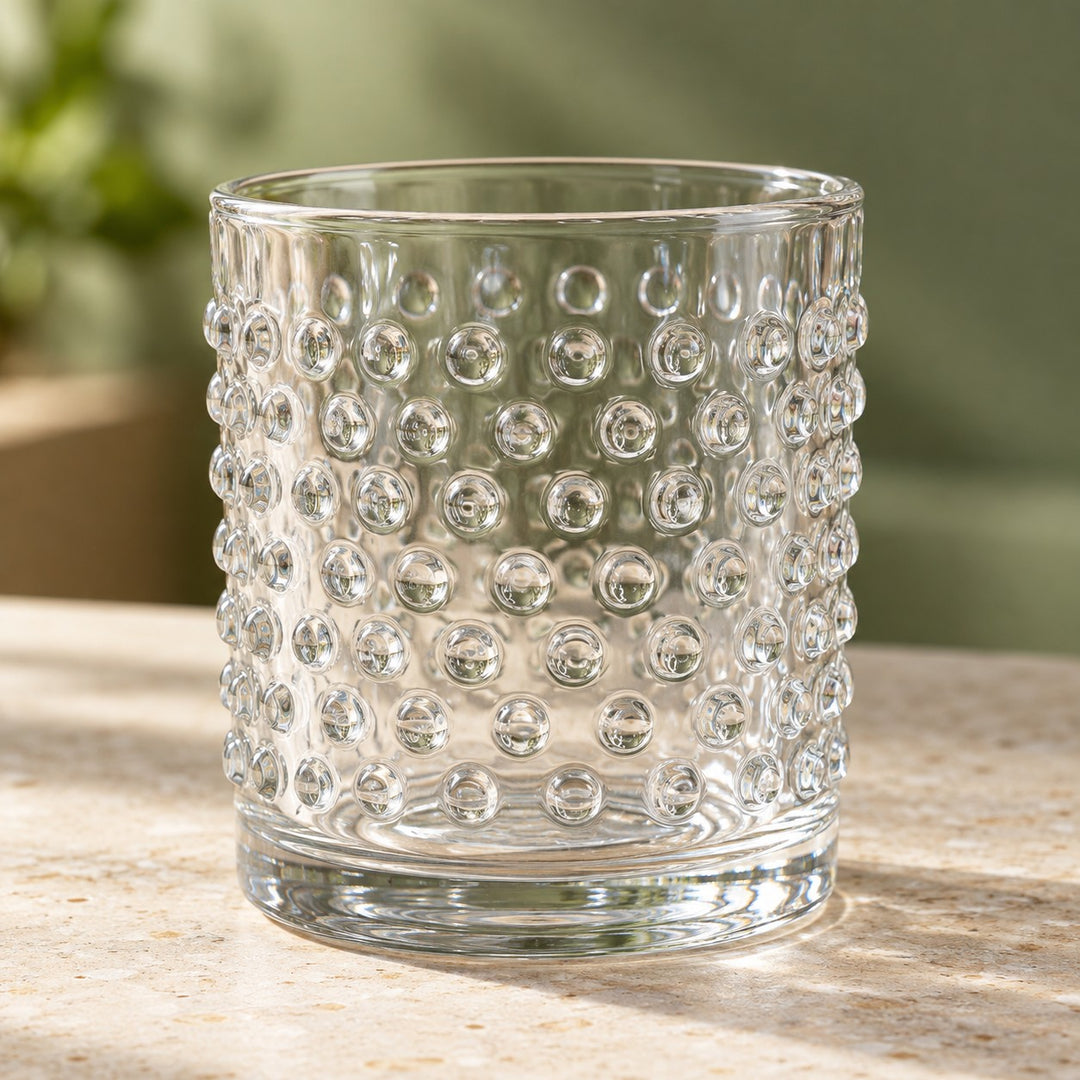 Clear embossed dot drinking glass stands on a stone counter, showing its raised vintage texture.