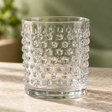 Clear embossed dot drinking glass stands on a stone counter, showing its raised vintage texture.