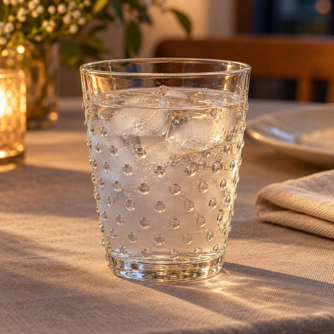 Clear embossed dot drinking glass holds chilled water on a softly lit dining table.