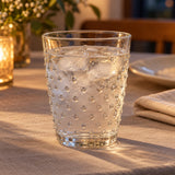 Clear embossed dot drinking glass holds chilled water on a softly lit dining table.