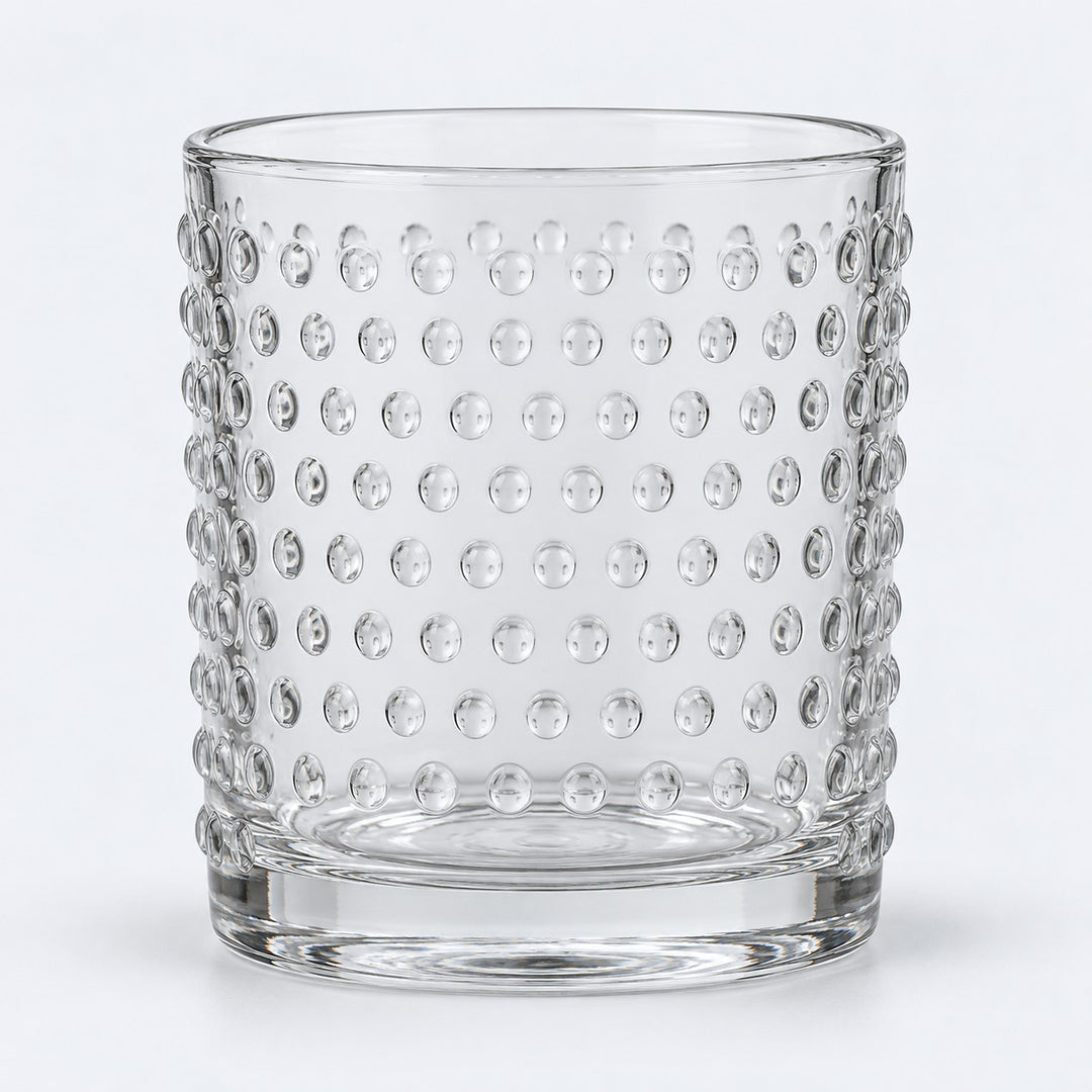 Clear embossed dot drinking glass centered on a pale gray studio background.