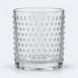 Clear embossed dot drinking glass centered on a pale gray studio background.