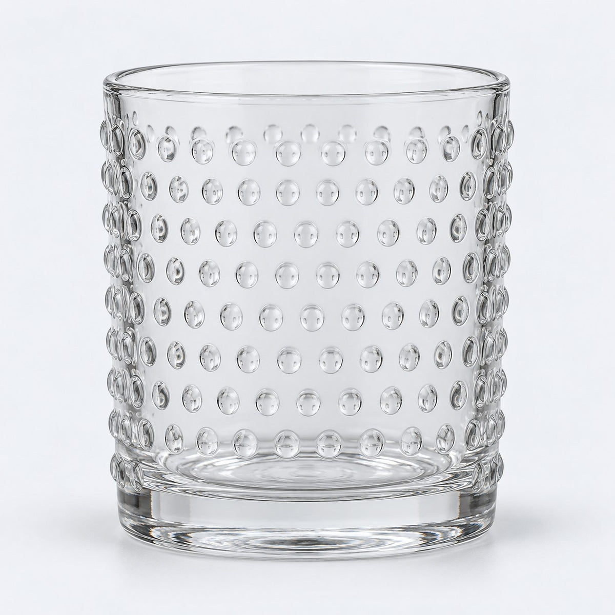 Clear embossed dot drinking glass centered on a pale gray studio background.