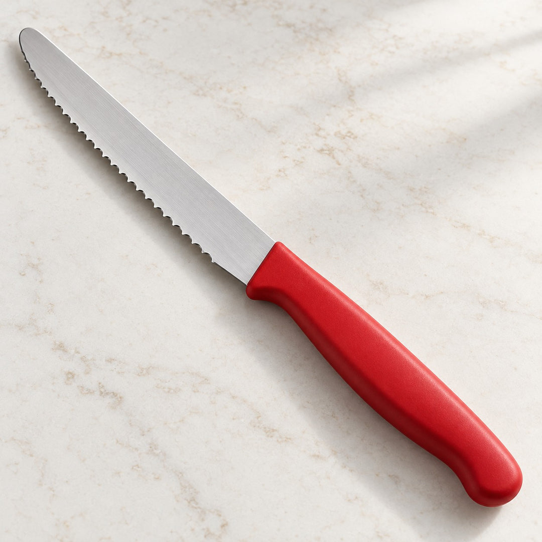 A red Serrated Steak Knife shows its fine serrated blade and rounded tip on a light surface.