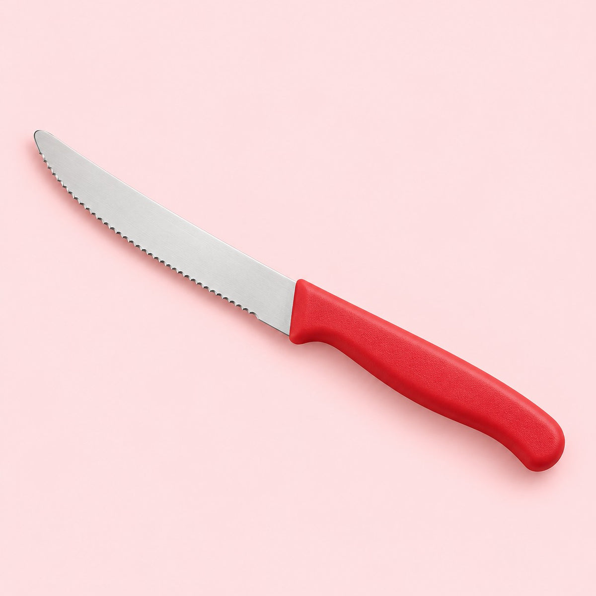 A red Serrated Steak Knife with a rounded stainless steel blade on a pale red studio backdrop.