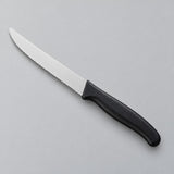 A black Serrated Steak Knife with a rounded stainless steel blade on a pale gray studio backdrop.