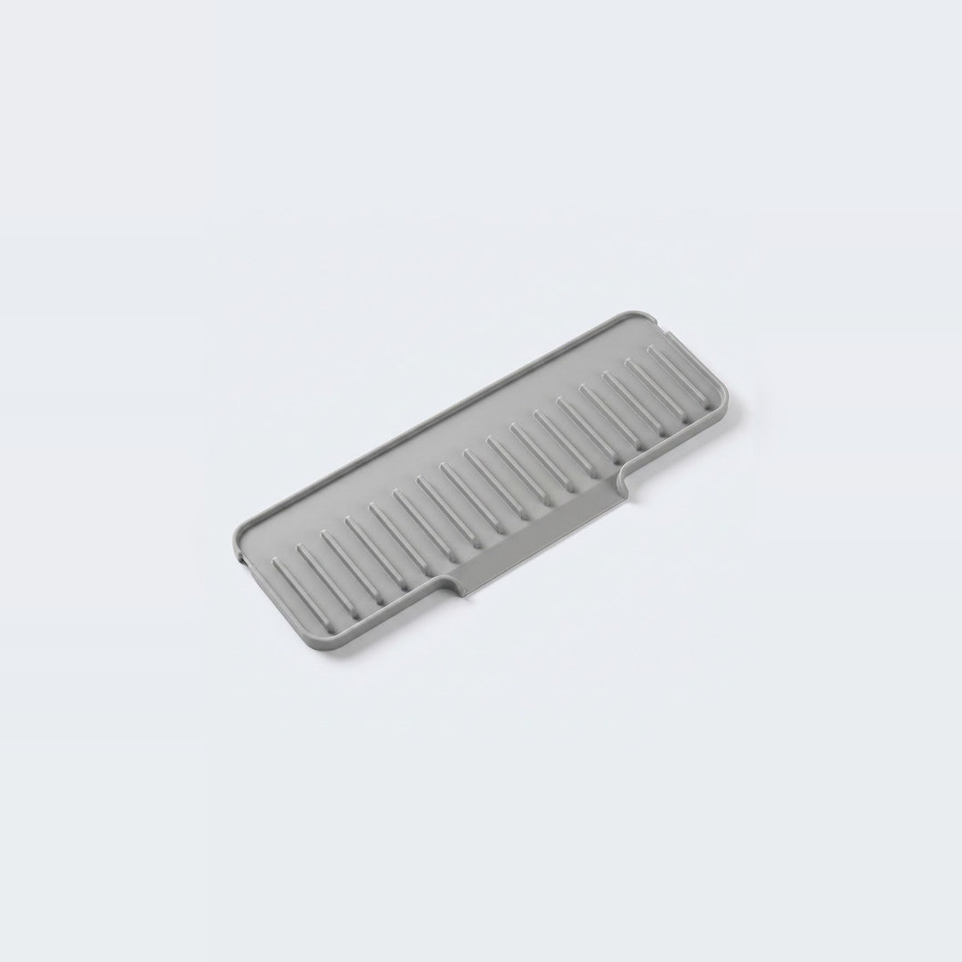 A gray silicone kitchen utensil, specifically a draining rack or strainer with parallel slotted channels, shown on a clean light gray background.