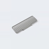 A gray silicone kitchen utensil, specifically a draining rack or strainer with parallel slotted channels, shown on a clean light gray background.