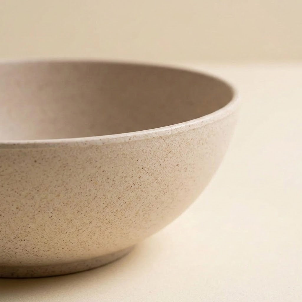 A close-up of a speckled beige ceramic bowl with a matte finish, set against a matching warm beige background.