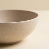 A close-up of a speckled beige ceramic bowl with a matte finish, set against a matching warm beige background.