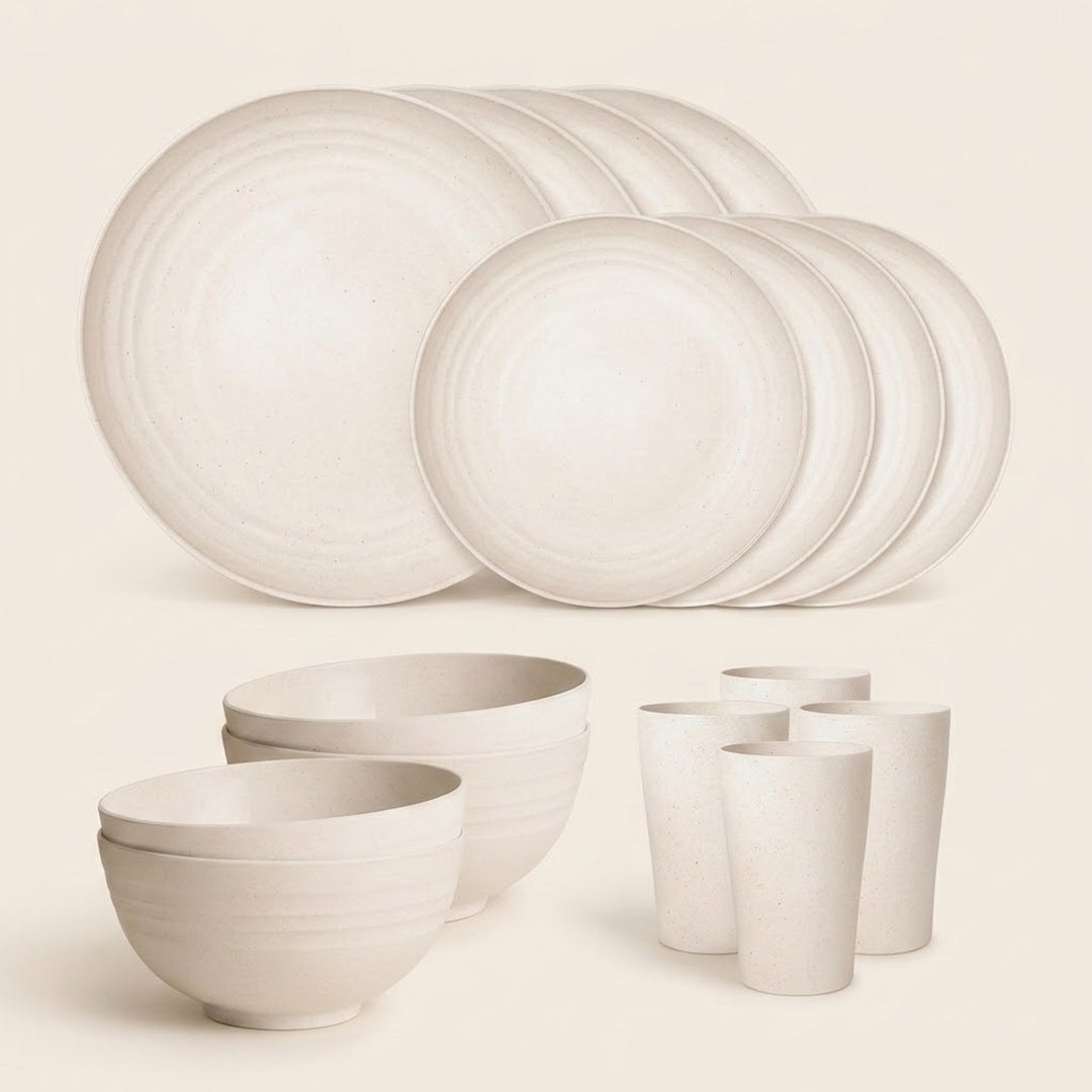 A coordinated ceramic tableware set in a warm off-white/cream tone, including large plates, bowls, stacked bowls, and tumbler cups, arranged on a plain light beige background.