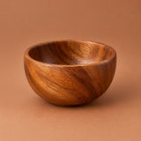 Small 225 ml acacia wood salad bowl centered on a warm tinted studio backdrop.