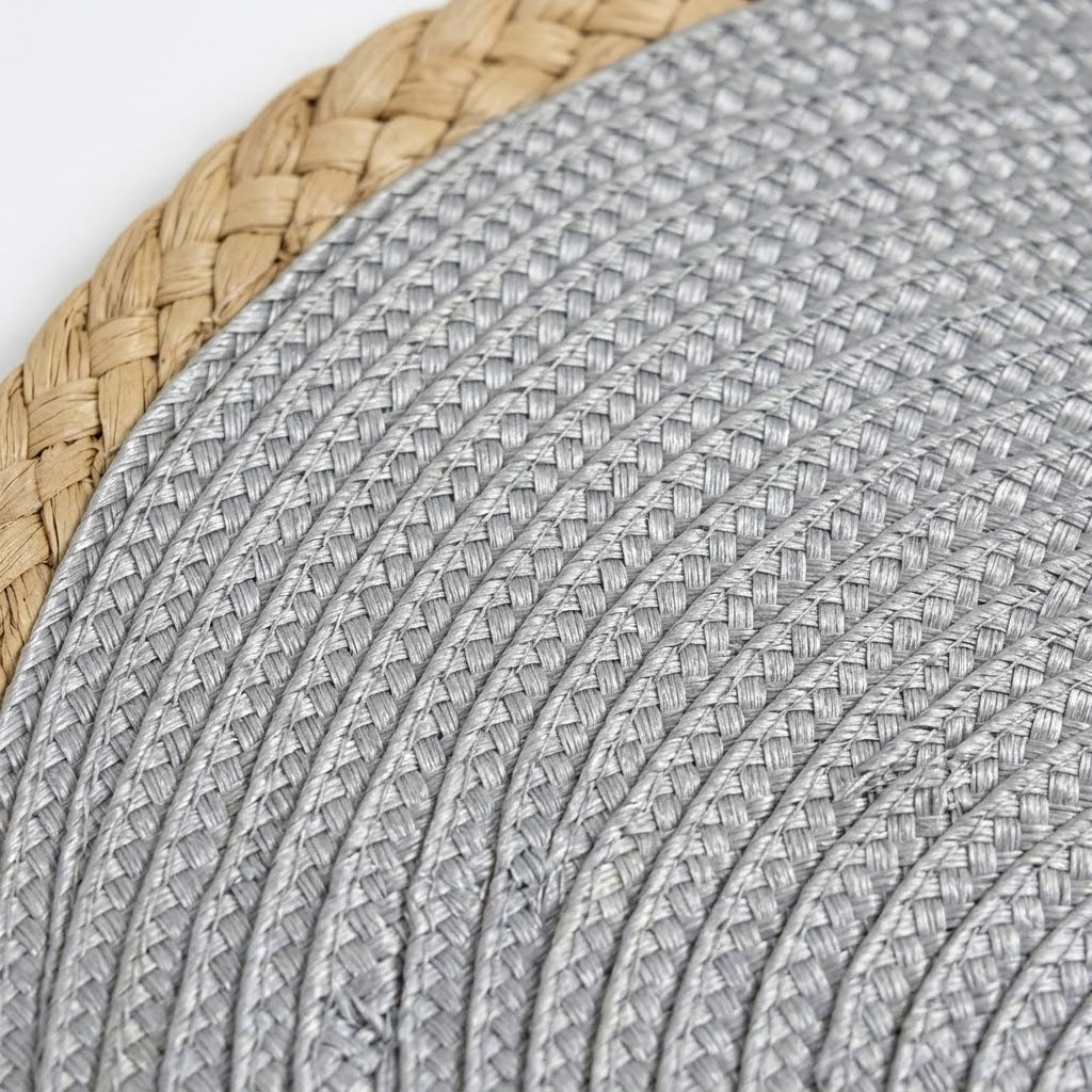 Close-up of a woven round placemat or tray, showing a light gray braided center and a natural tan straw border on a white background.