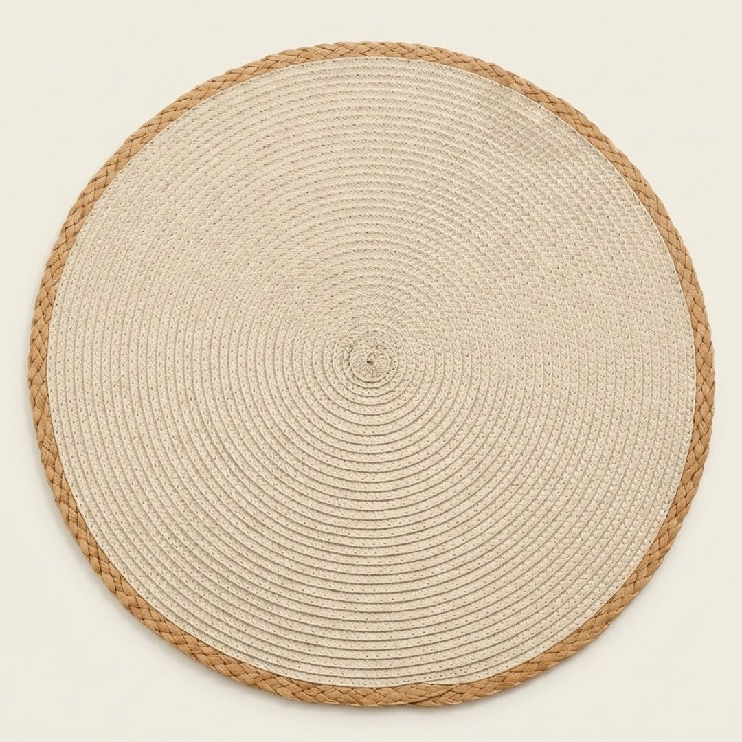 A round woven placemat or rug made of natural beige rope with a braided tan border, photographed from directly above on a light cream background.
