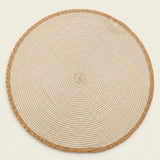 A round woven placemat or rug made of natural beige rope with a braided tan border, photographed from directly above on a light cream background.