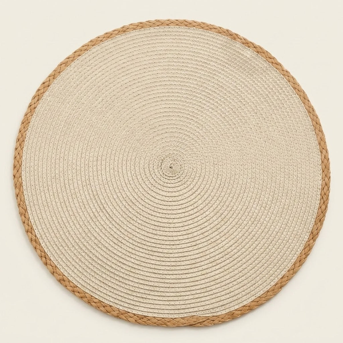 A round woven placemat or rug made of natural beige rope with a braided tan border, photographed from directly above on a light cream background.