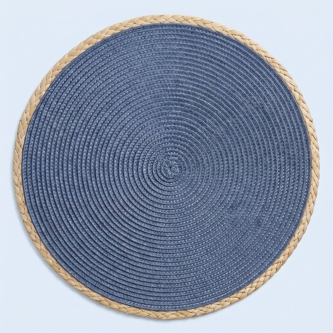 A round braided placemat with a textured blue center and a natural beige rope border, shown from a top-down view on a light blue background.