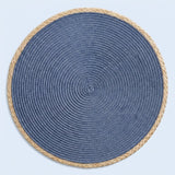 A round braided placemat with a textured blue center and a natural beige rope border, shown from a top-down view on a light blue background.