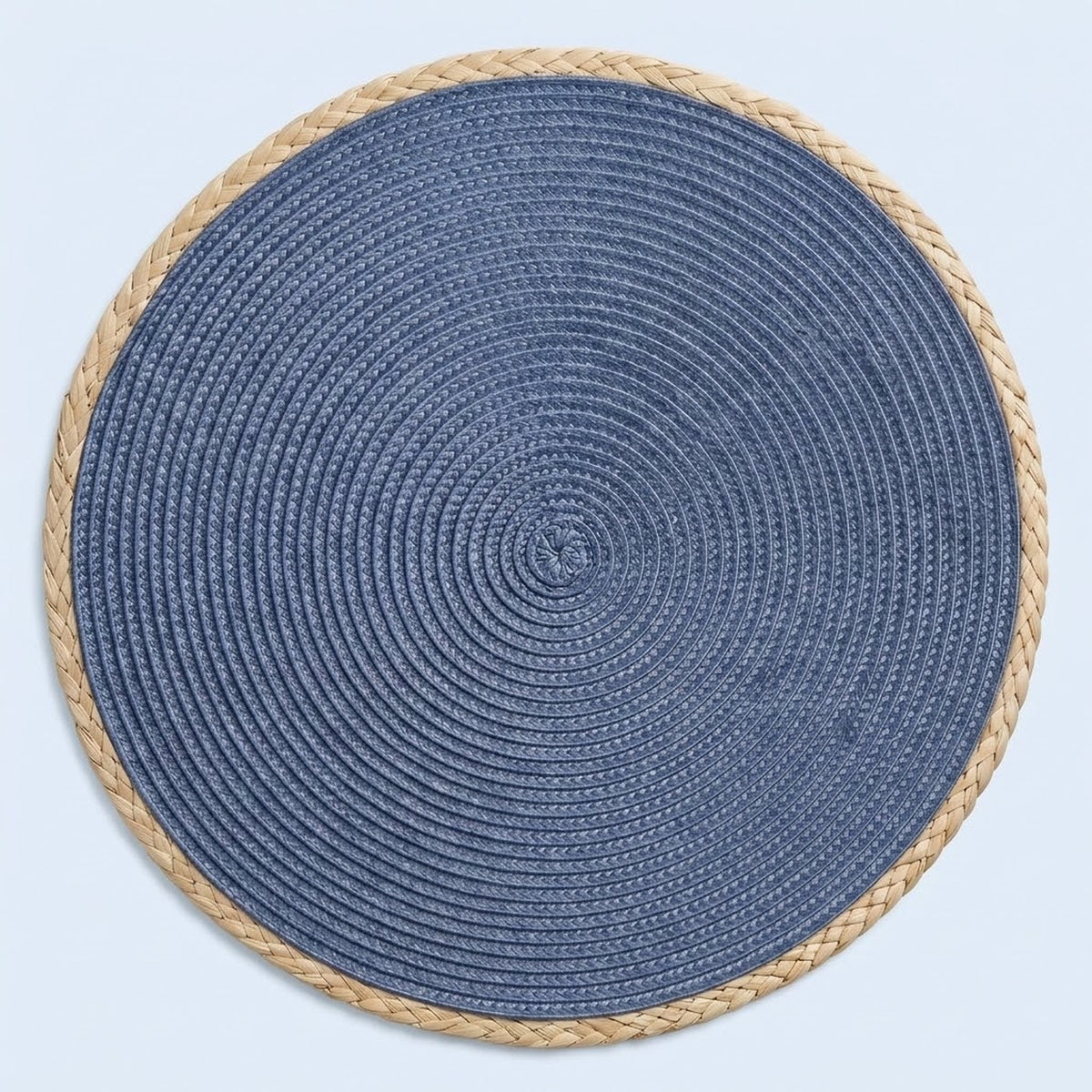A round braided placemat with a textured blue center and a natural beige rope border, shown from a top-down view on a light blue background.