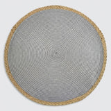 A round woven placemat with a textured silver-gray center and a natural tan braided border, shown flat against a light gray background.