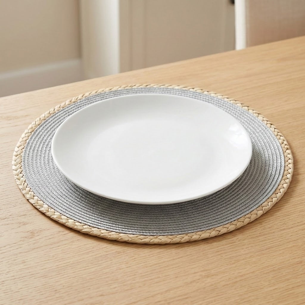 A white ceramic plate layered on top of a round woven placemat with a gray center and natural straw border, set on a light wood table.