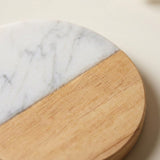 A close-up of a round coasters or trivets made of a two-tone material, featuring a white marble half and a light natural wood half.