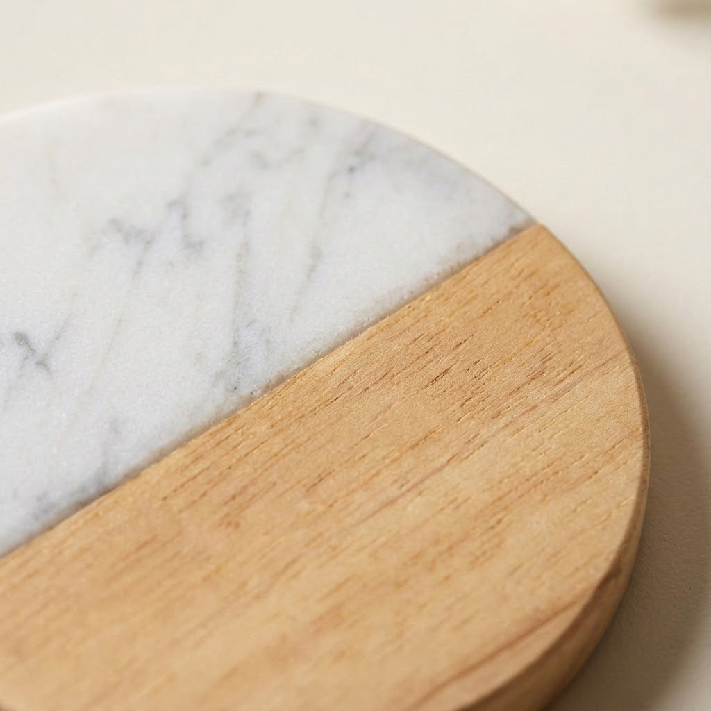 A close-up of a round coasters or trivets made of a two-tone material, featuring a white marble half and a light natural wood half.