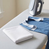 A folded white fabric item sits on a light gray ironing board next to a blue garment with a white neck trim, with a white and gray iron in the background.