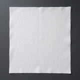 A square white fabric cloth or napkin with slightly raw edges, laid flat on a dark gray textured background.