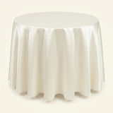 A round table covered with a smooth, draped ivory satin tablecloth, shown against a solid cream background.